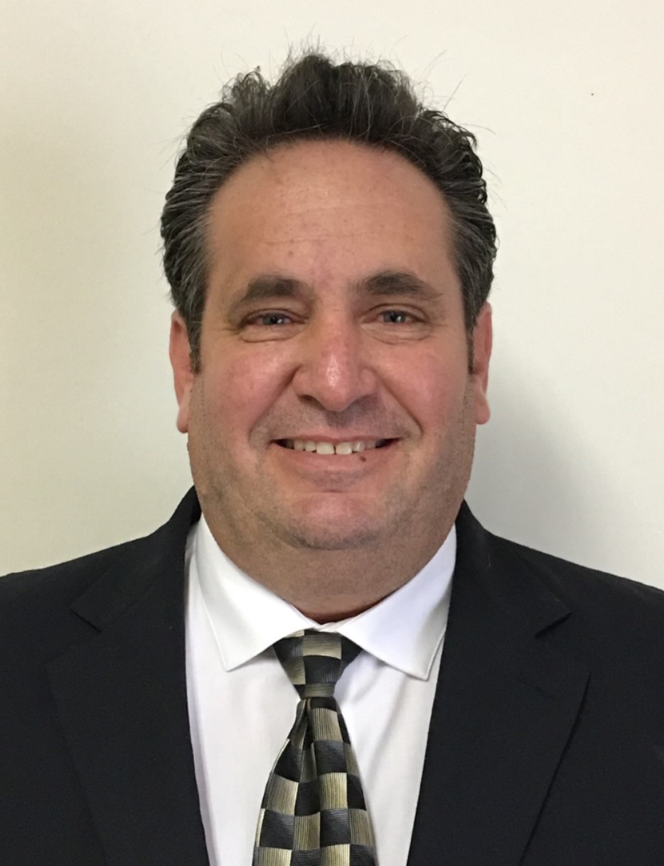 A person wearing a suit and tie smiling at the camera Description generated with very high confidence